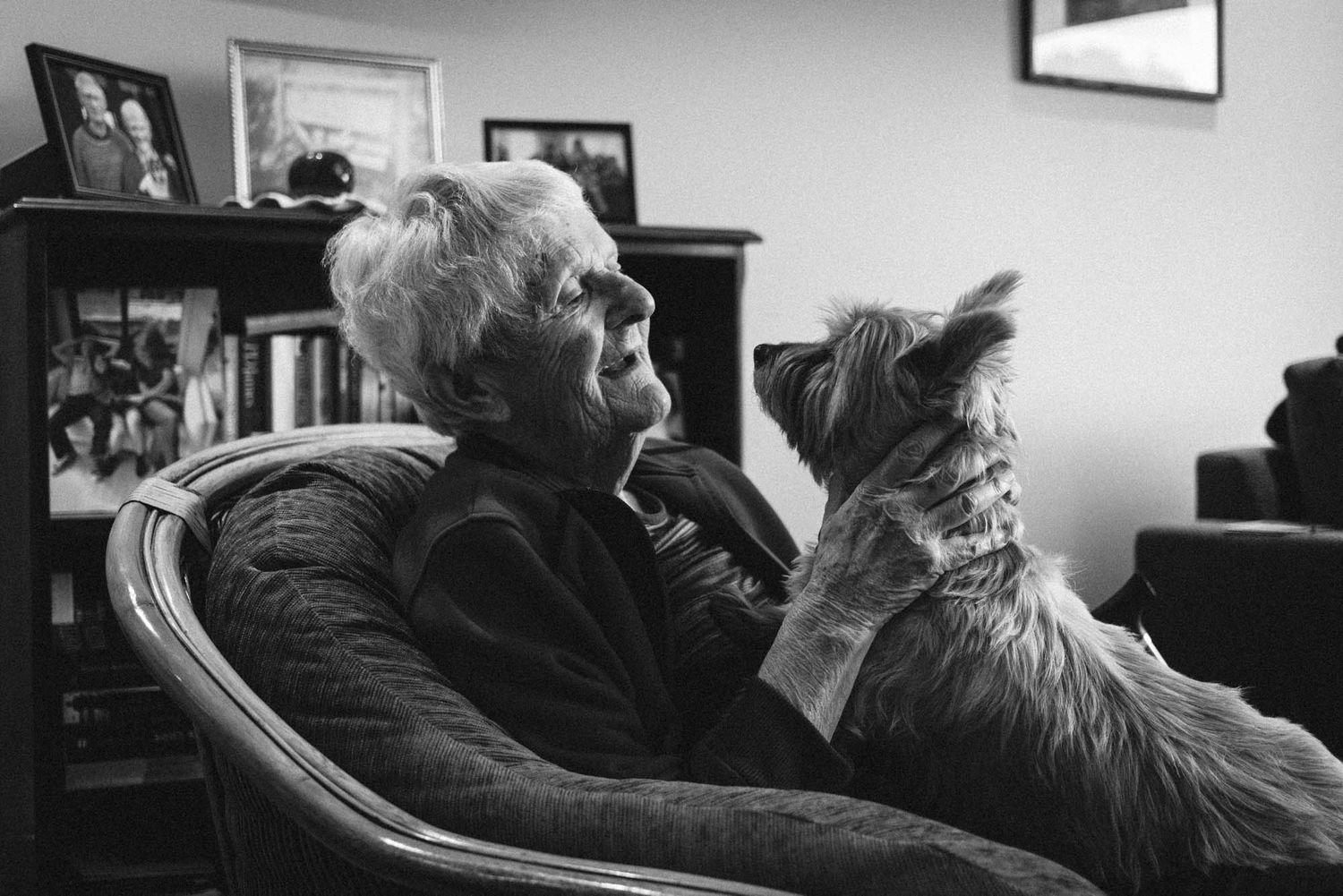 Black and white image showing an elderly person resting in a chair with her small terrier.