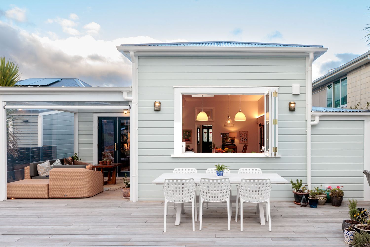 Modern white house exterior with outdoor seating and panoramic windows.