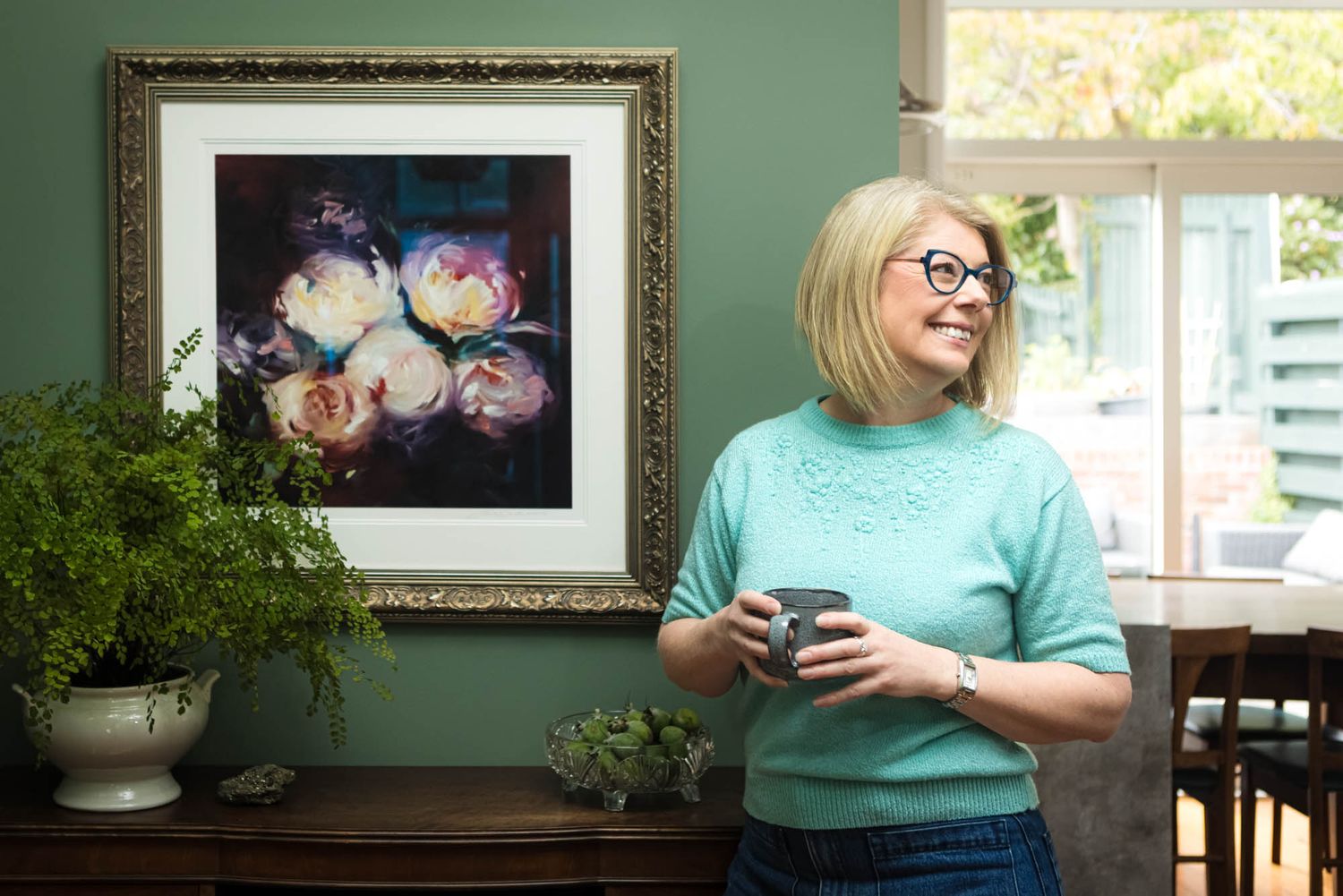 Interior room with green walls displaying framed artwork and floral arrangements.