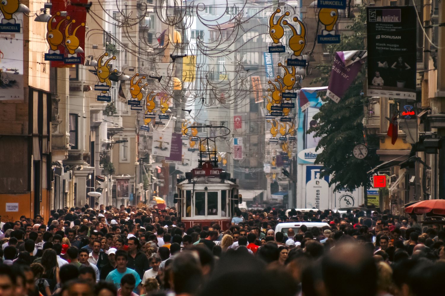 Busy urban street scene in Istanbul with crowds and storefronts under decorative lighting.