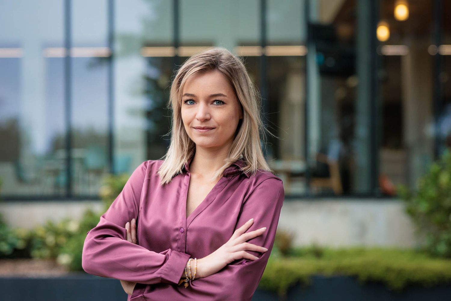 Professional in pink blouse standing with arms crossed outside modern building.