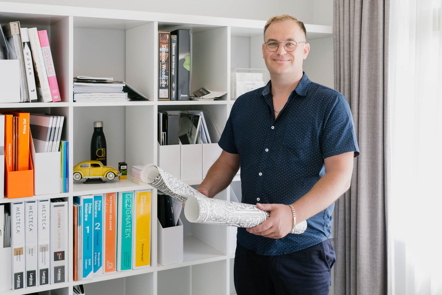 Person holding architectural plans in modern office with white shelving.