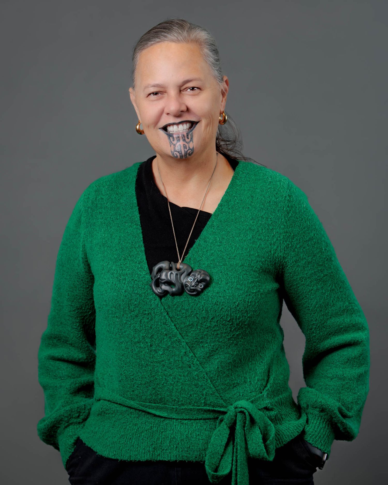Professional portrait showing a person in a bright green sweater against a gray studio background.