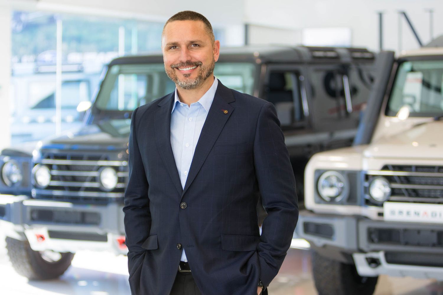 Armstrong's staff member standing in front of luxury vehicles in a modern car showroom.