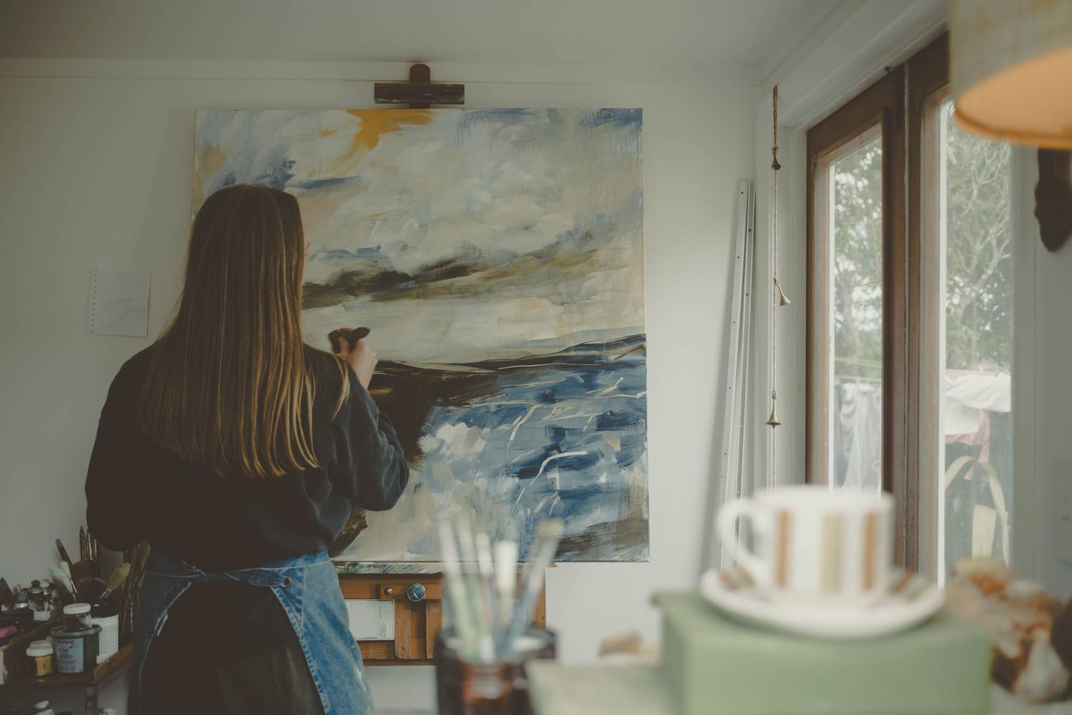 Artist painting a seascape on canvas in a bright studio with natural light.