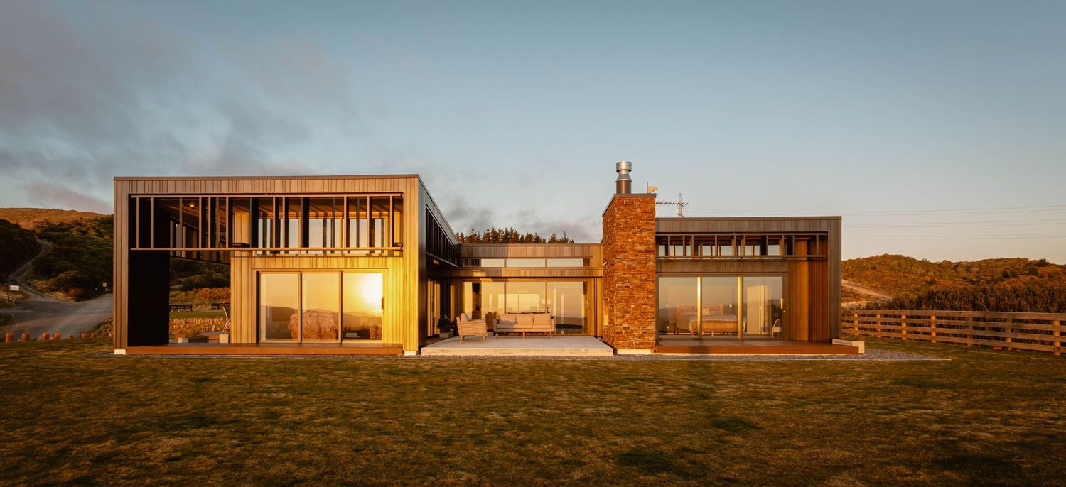 Contemporary lifestyle house design with metal cladding set against rolling hills at sunset.