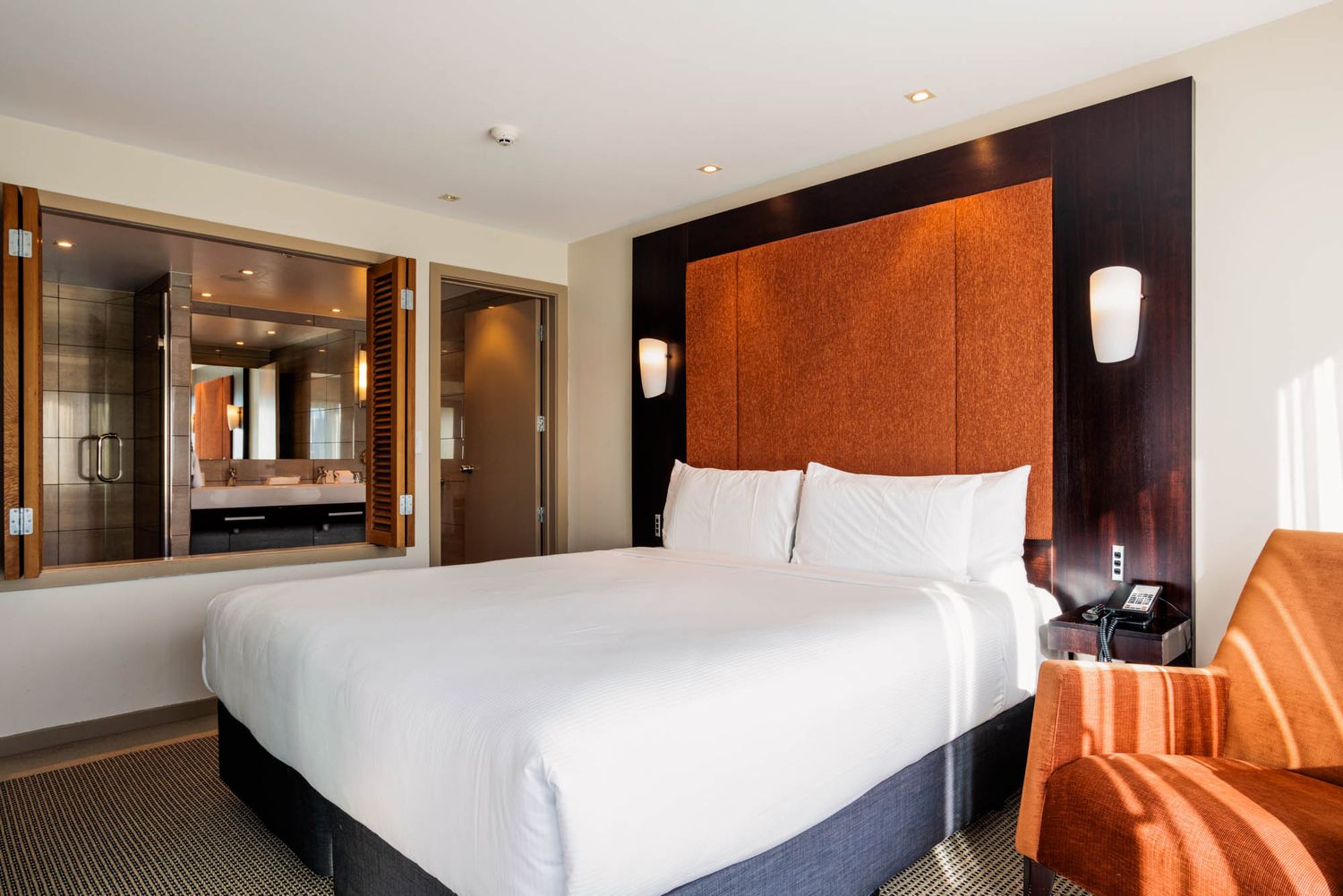 Luxury hotel room interior at Copthorne Hotel Wellington with white bedding and orange accent furniture.