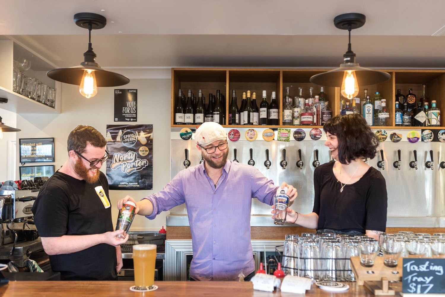 Three people socializing at a craft beer bar with tap handles, glowing pendant lights, and bottle displays.