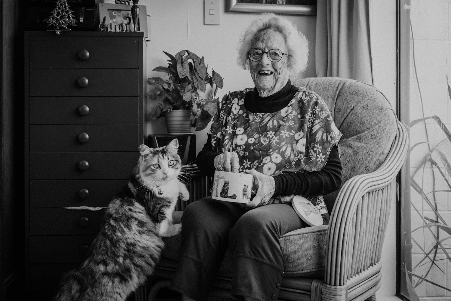 An elderly person relaxes in a chair at home with her cat nearby.