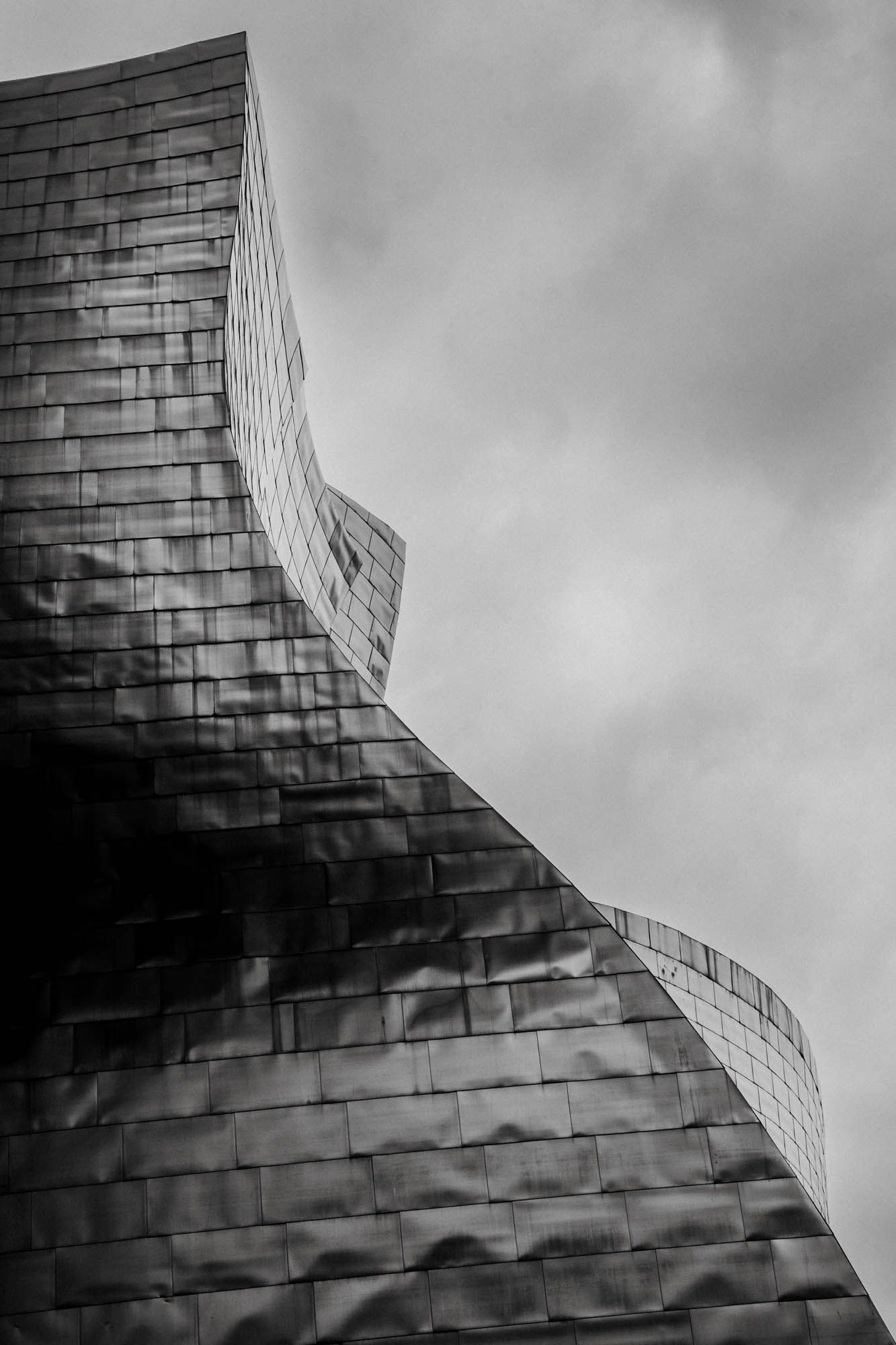 Guggenheim Bilbao facade with geometric patterns photographed in black and white against cloudy sky.