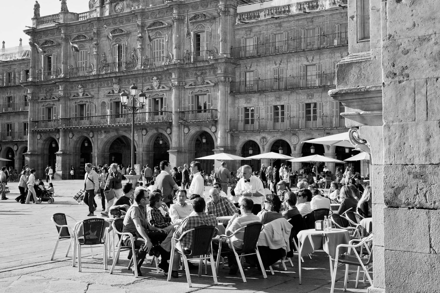 Historic stone arcade with outdoor cafe seating and umbrellas along a plaza in Salamanca.