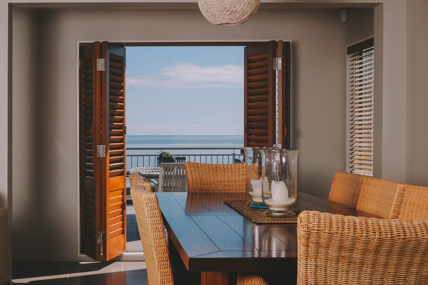Dining space with rattan chairs and ocean views through large picture windows.