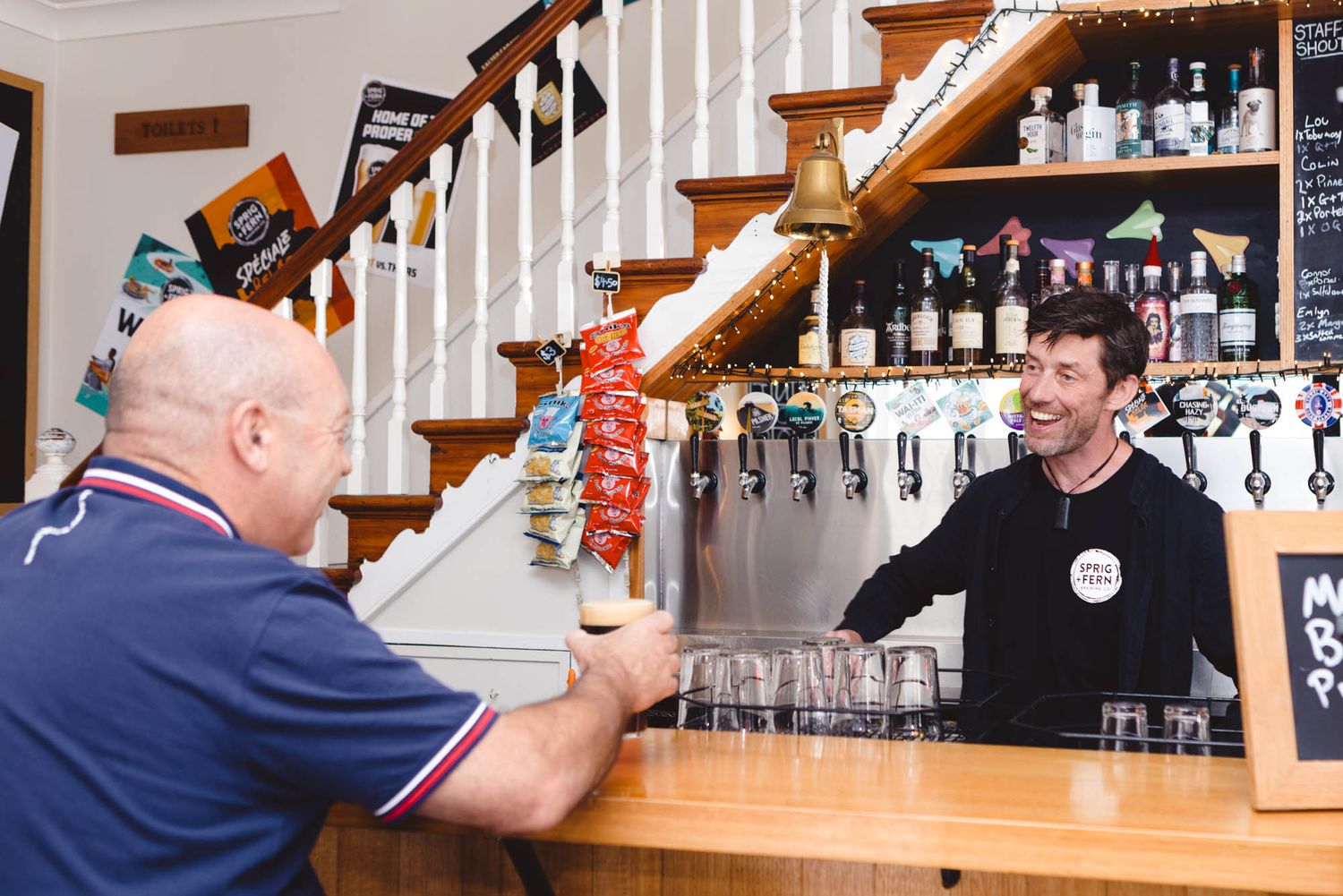Sprig and Fern bar counter with wooden staircase and shelves displaying bottles of spirits.