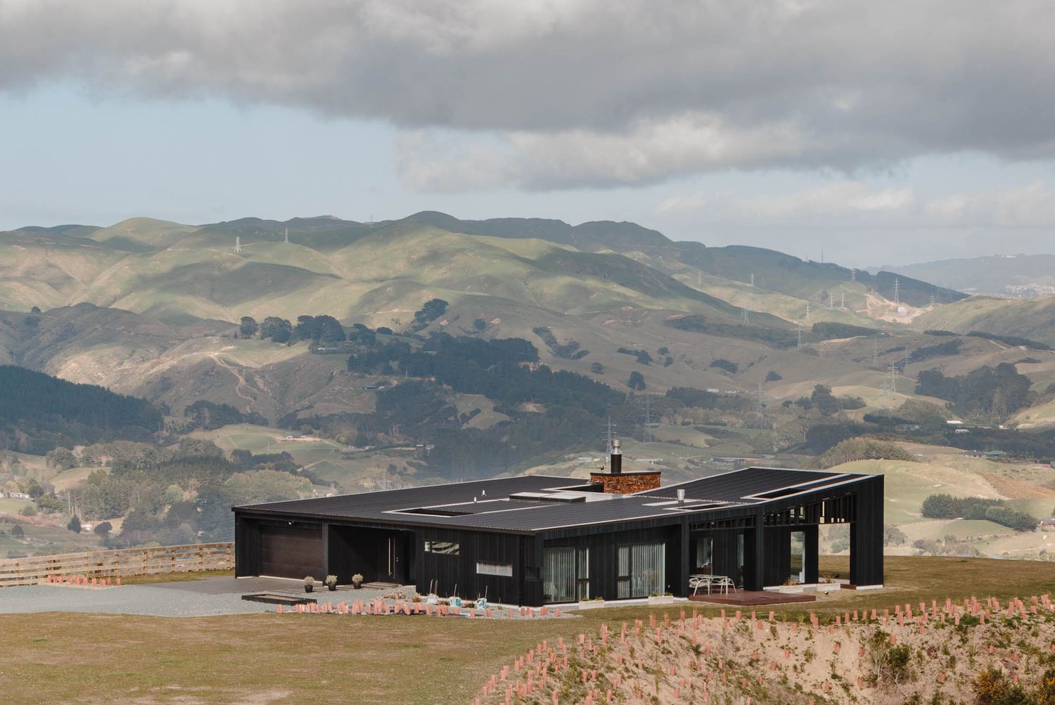 Modern black building set against rolling hills and cloudy mountain landscape.