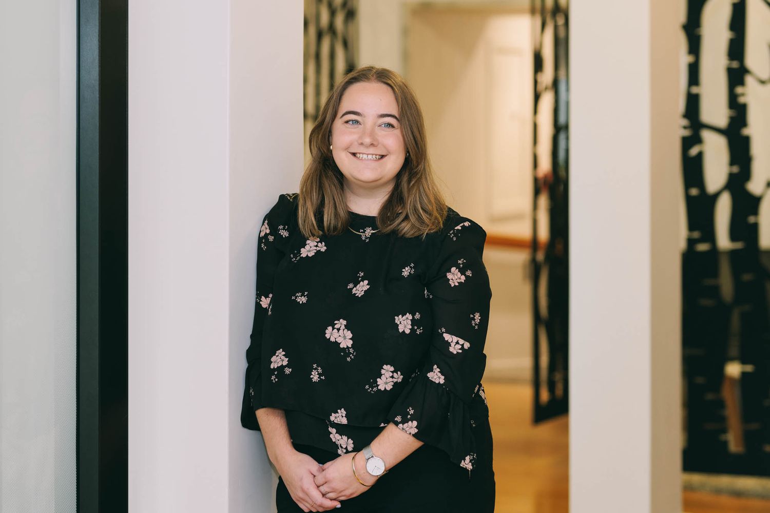 Professional in a black floral print top smiling in an office corridor.