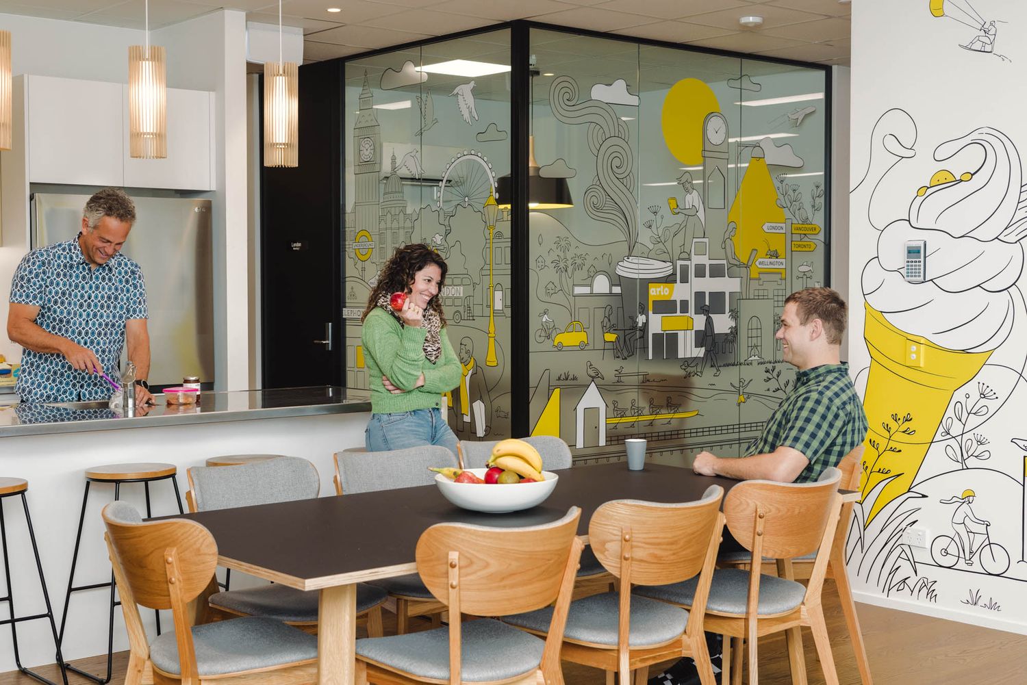 Office break area at Arlo with wooden chairs and creative wall murals in yellow and black.