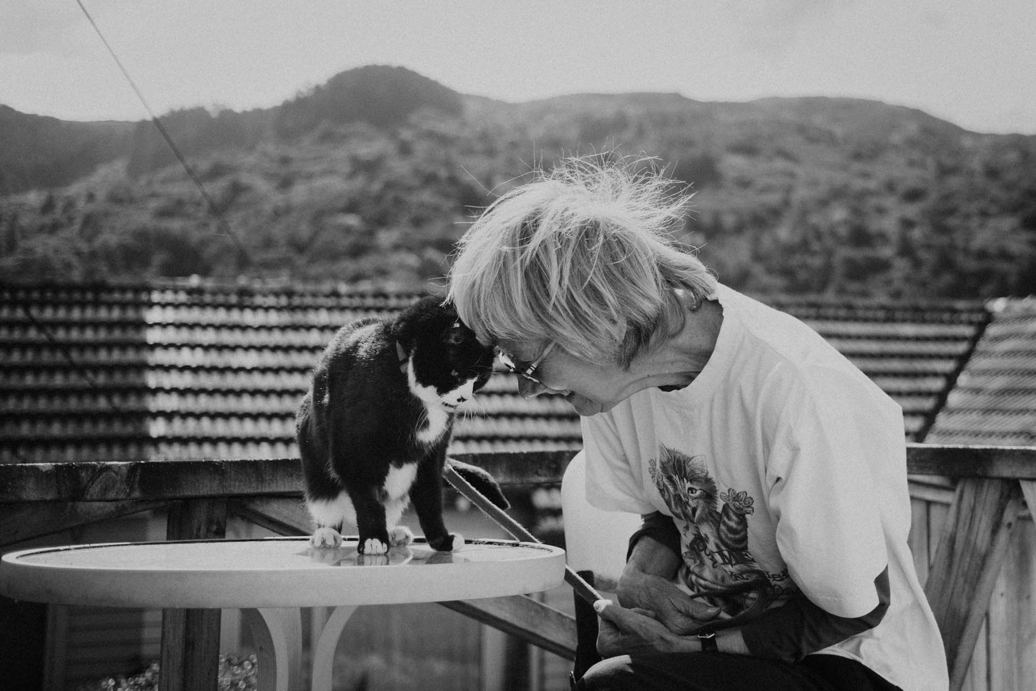 An elderly lady touching heads with her black and white cat.
