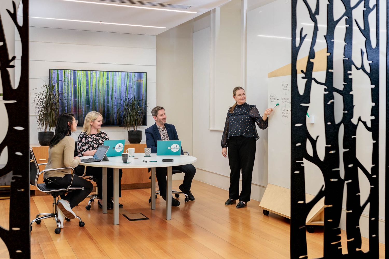 CoDigital office meeting in progress with tree-themed wall decor and modern furniture.