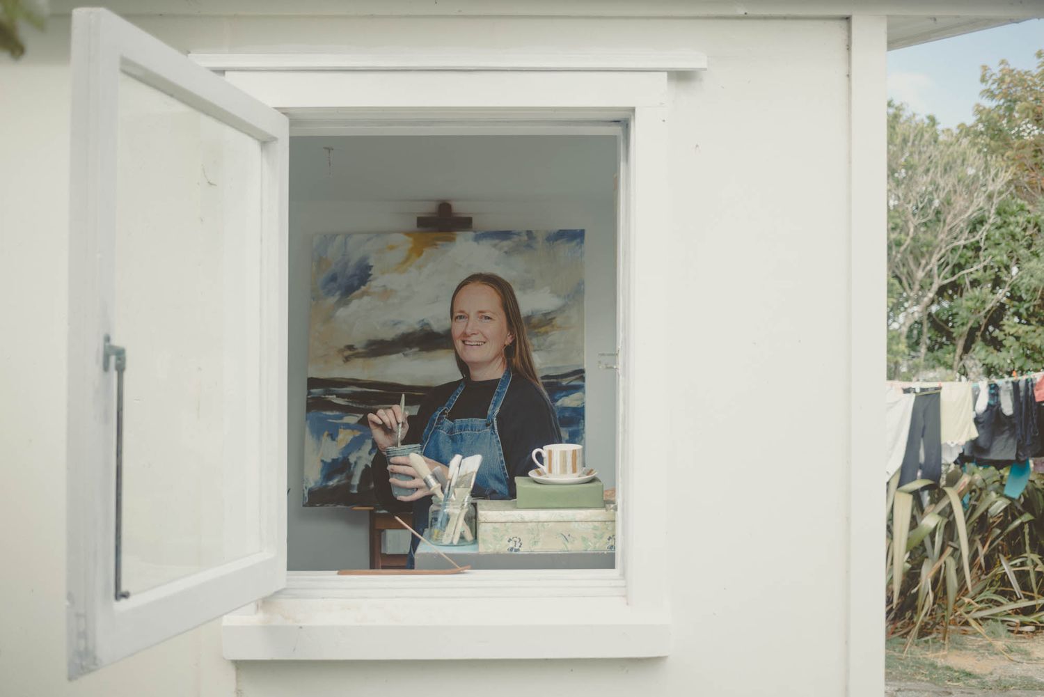 View through a window showing an art studio with paintings and supplies.