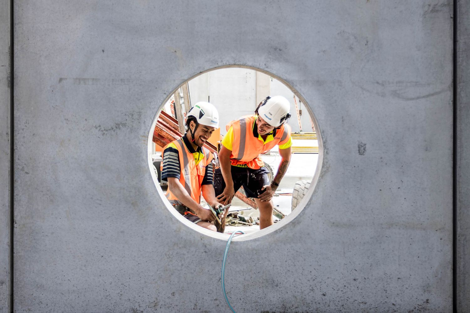 Concrete wall with circular cutouts showing glimpses of activity of Maycroft Construction workers through the openings.