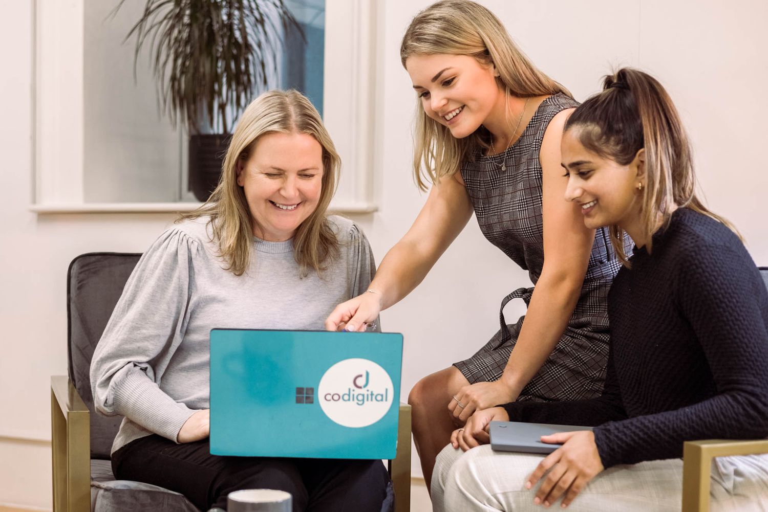 Three CoDigital colleagues collaborating while looking at laptop screen in office.