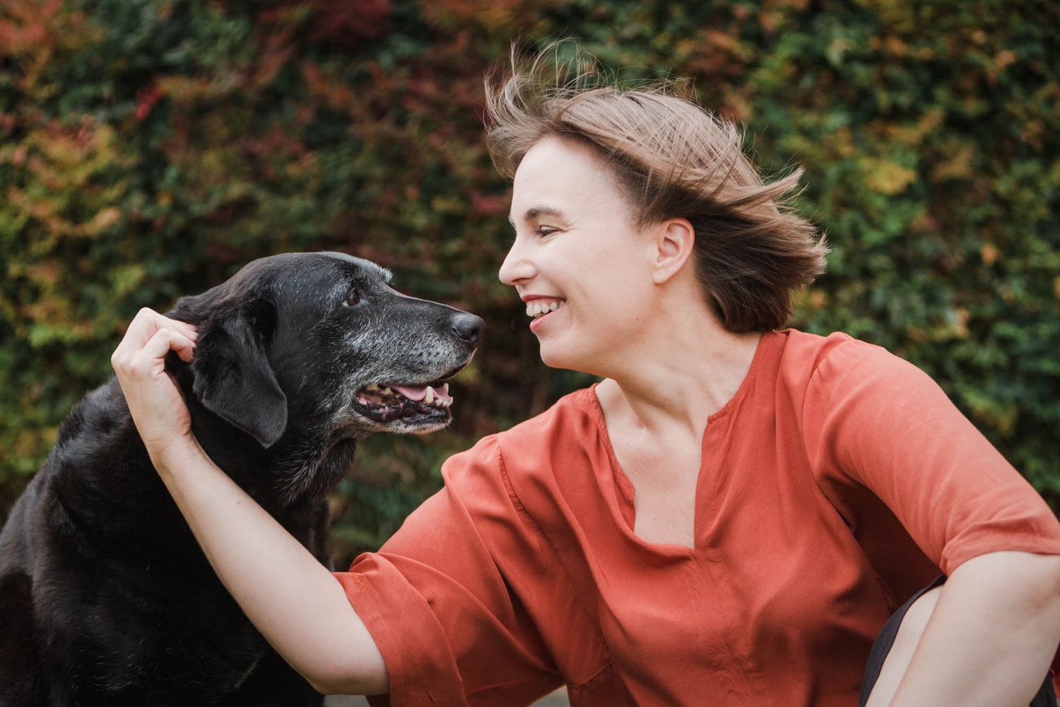 Candid moment between a person in coral clothing playing with her dog outdoors.