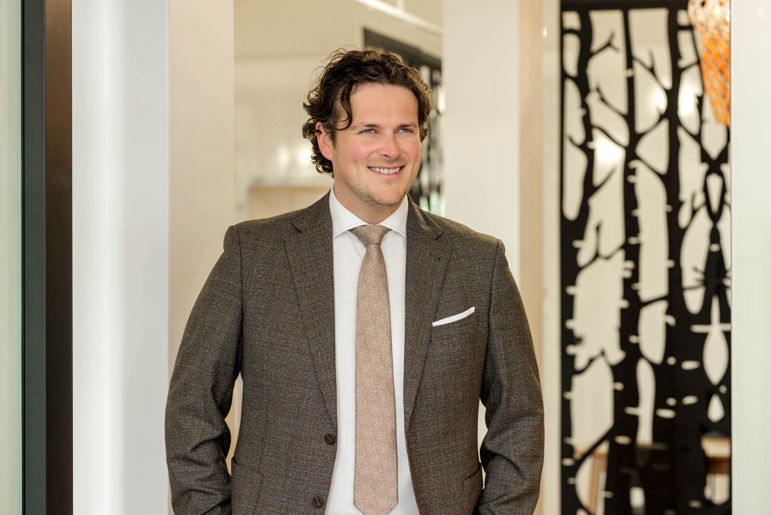 Business professional poses in a modern office hallway with artistic wall decorations.
