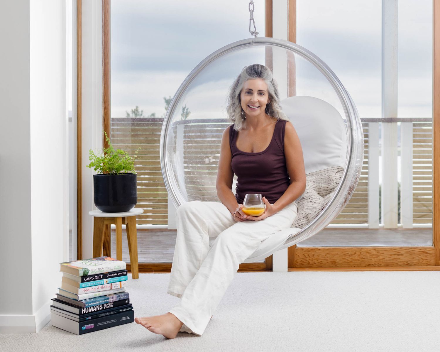 Jo Williment of Sage Studio in a contemporary living space featuring hanging bubble chair and window views.