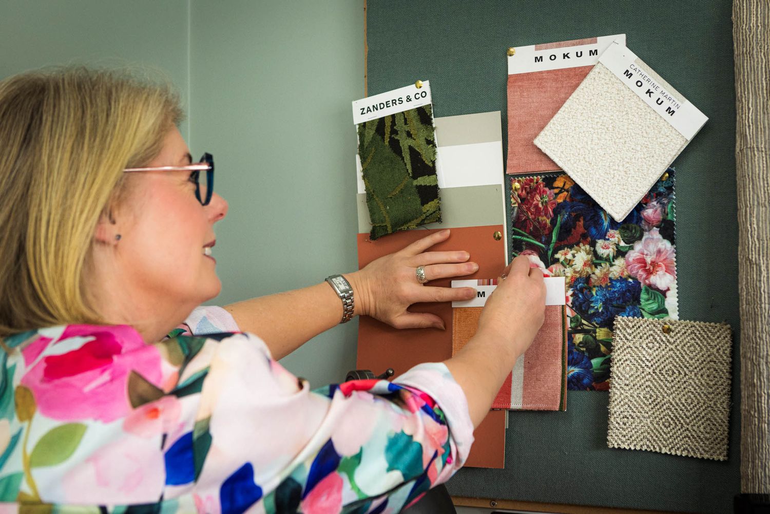 Person organizing papers and photos on a wall-mounted display board.
