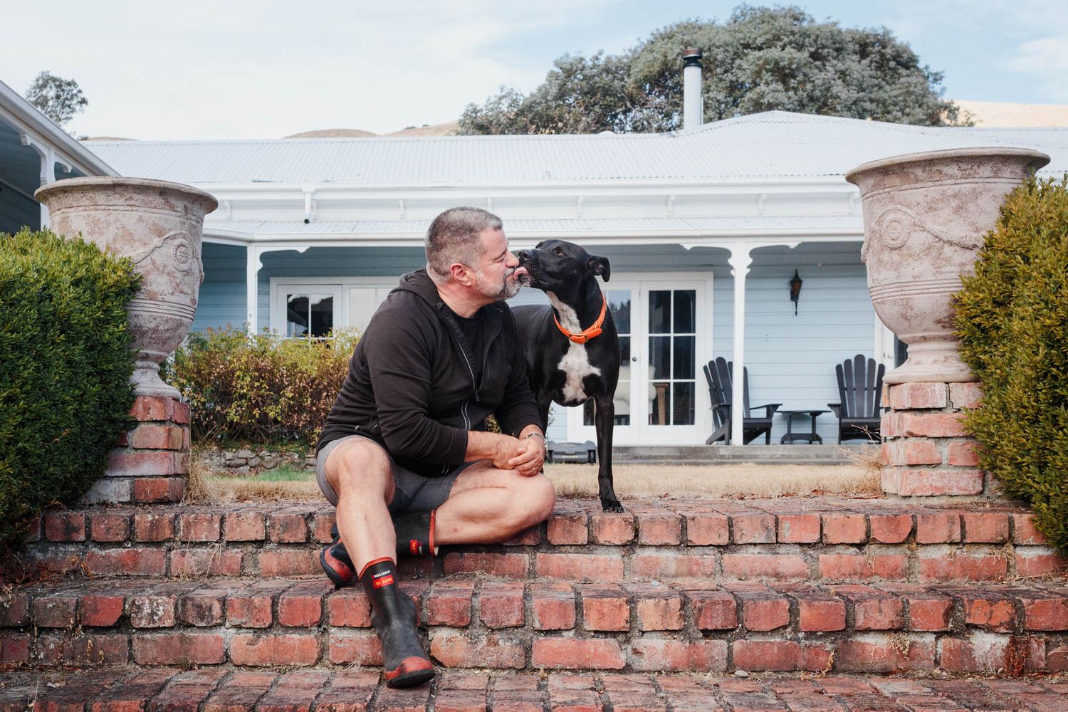 Person and dog sitting along a decorative brick wall outside a white house.