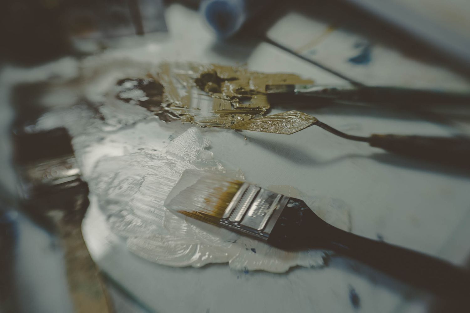 Paint brushes and mixing tools on a white paint-covered surface.