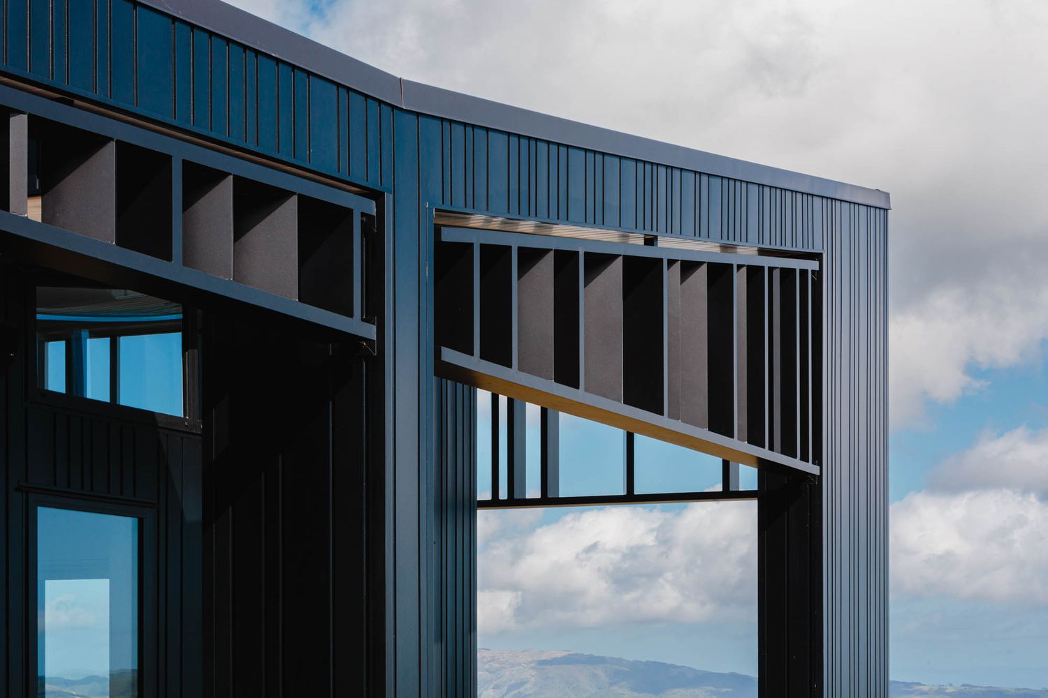 Contemporary dark-sided building with large windows and dramatic angular roofline against cloudy sky.