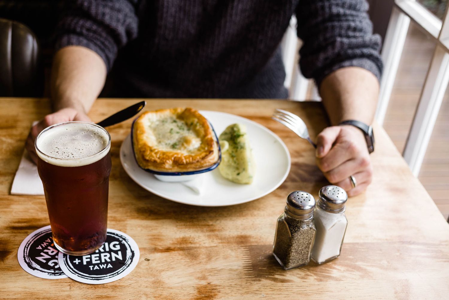 Close-up of craft beer glasses and plates on a rustic wooden table at Sprig and Fern Tavern.