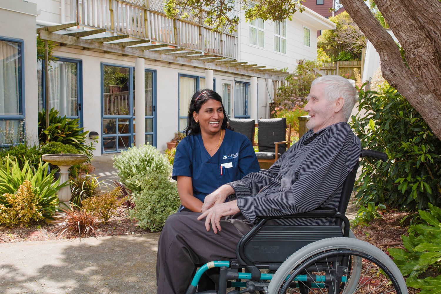 People conversing on an outdoor patio surrounded by lush garden landscaping.