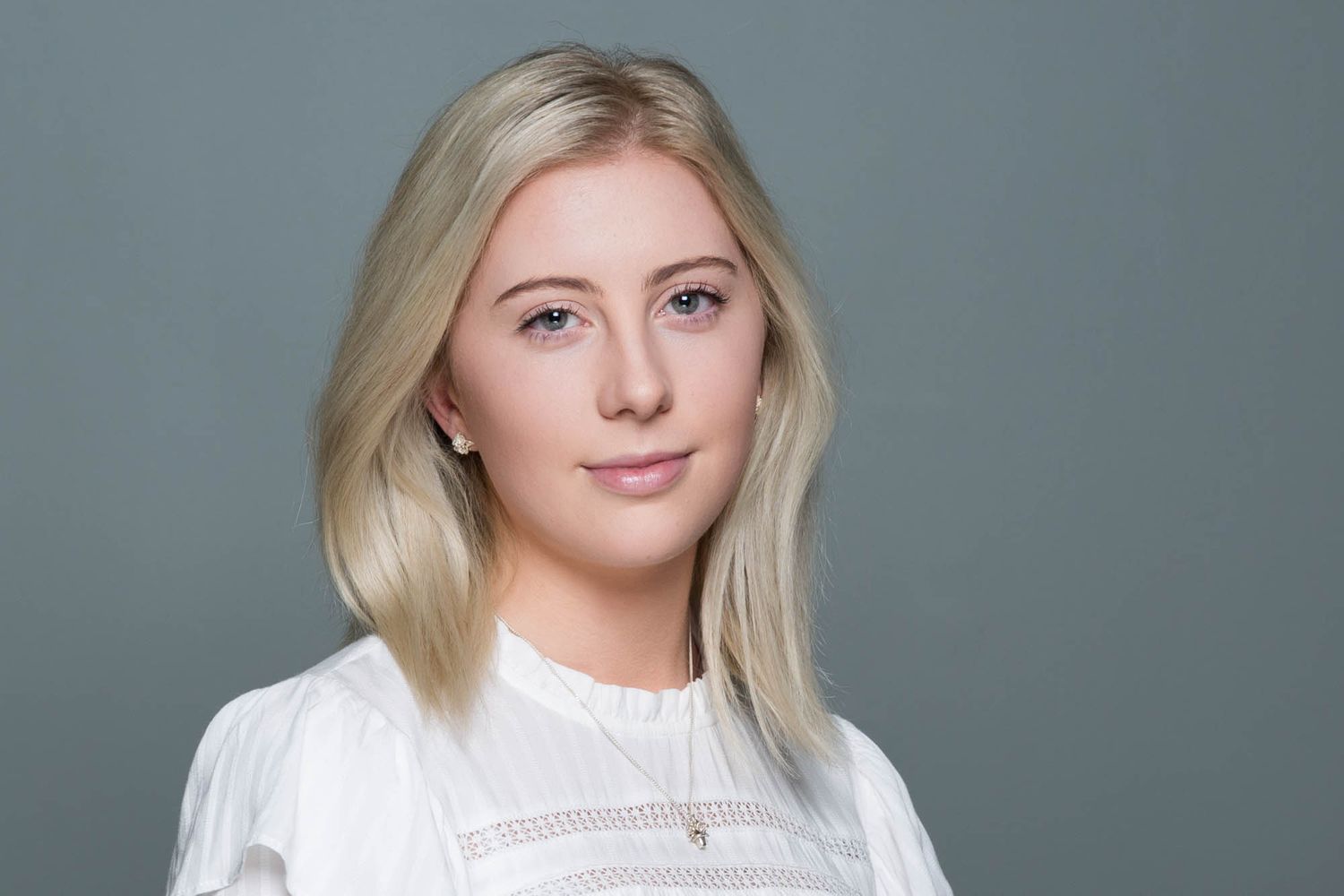 Professional headshot against grey background wearing white top.
