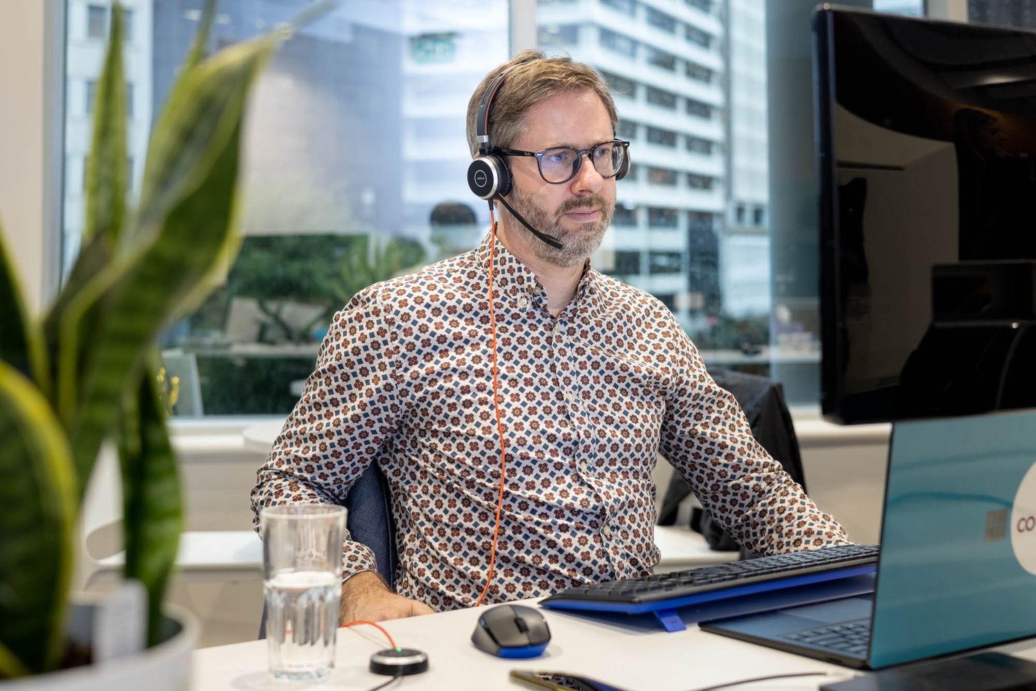 Professional wearing headset working at modern desk with laptop and plant.