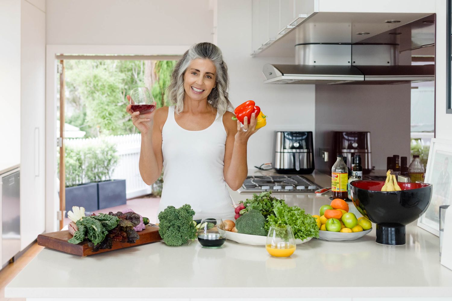 Modern kitchen with fresh produce and beverages displayed on white countertops.