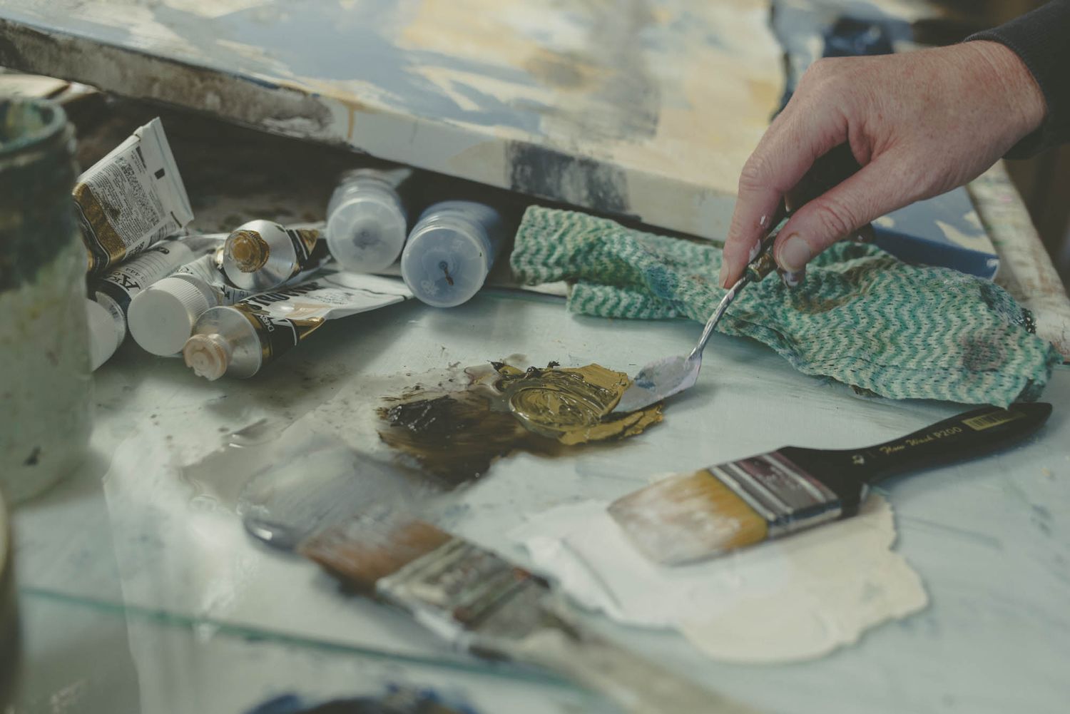 Close-up of hands mixing paint colors on an artist's palette.