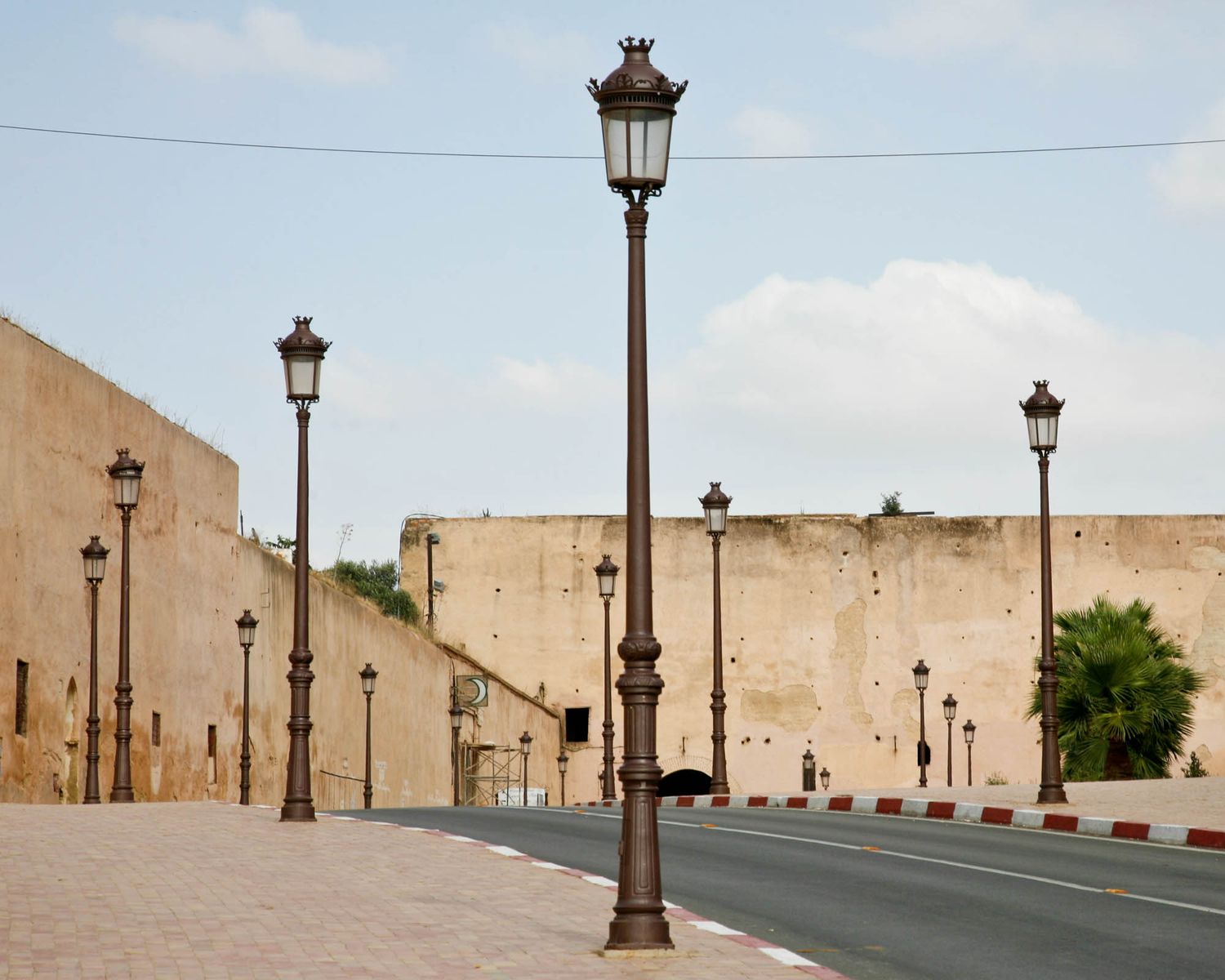 Row of vintage street lamps along empty stone wall under blue sky in Meknes.