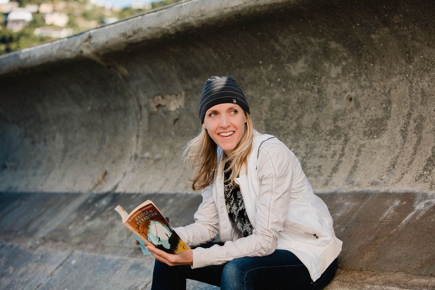 Person sitting outdoors reading a book against concrete wall.