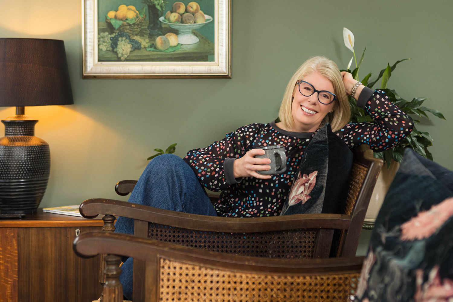 Person relaxing in vintage cane chair with drink in cozy living room setting.