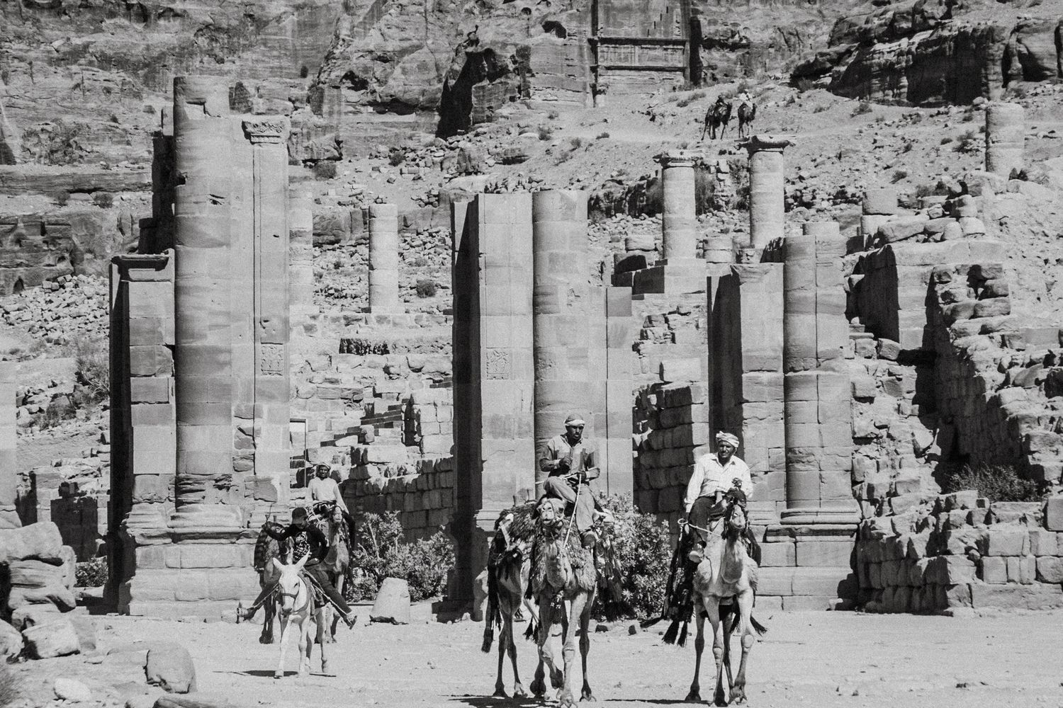 Historic stone ruins in Petra with weathered walls and archways filled with visitors.