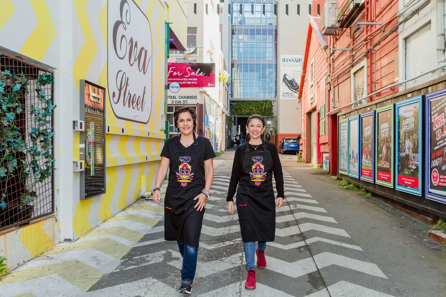 Two chefs walking down a colorful Wellington urban alleyway wearing matching black t-shirts.