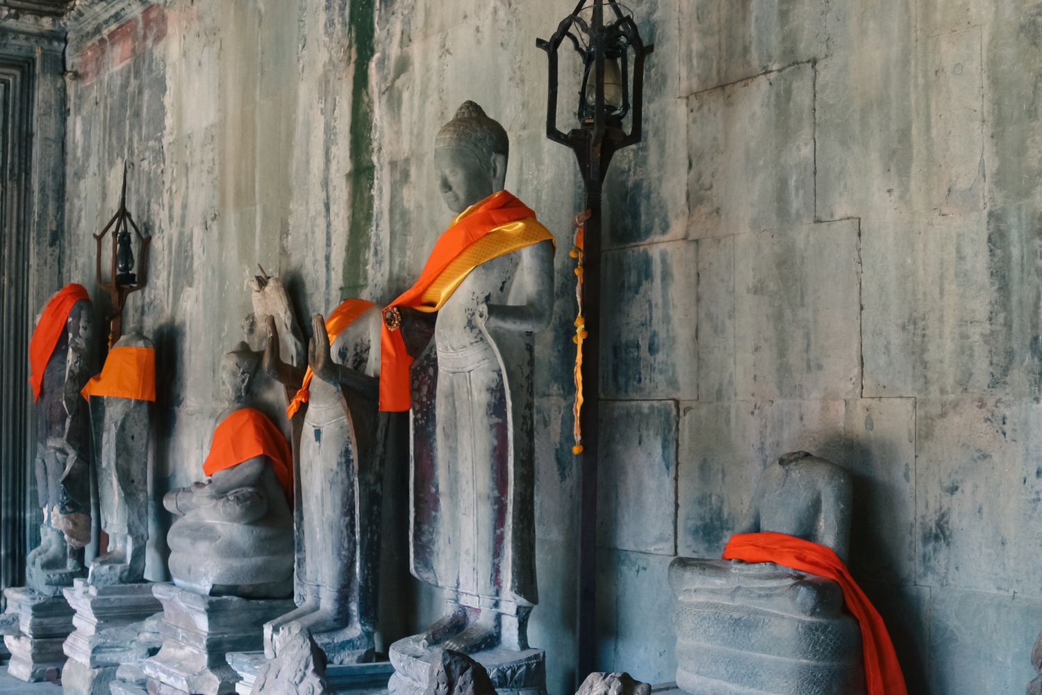 Ancient stone corridor in Angkor Wat with lanterns and orange-robed figures creating an atmospheric scene.