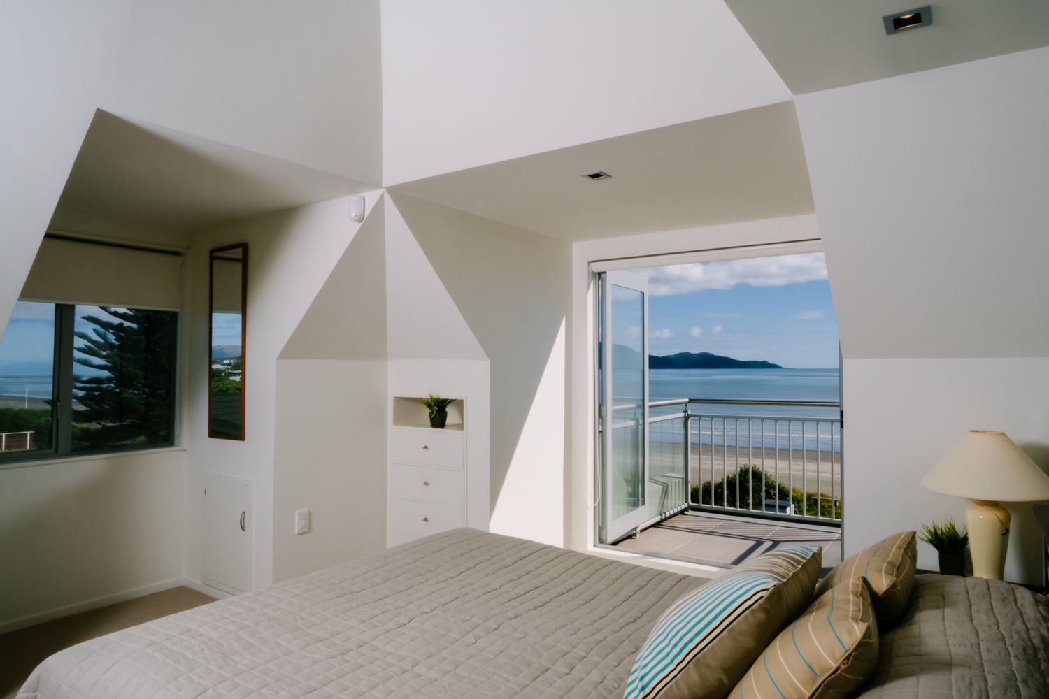 Minimalist bedroom with angular walls and large window framing ocean view.