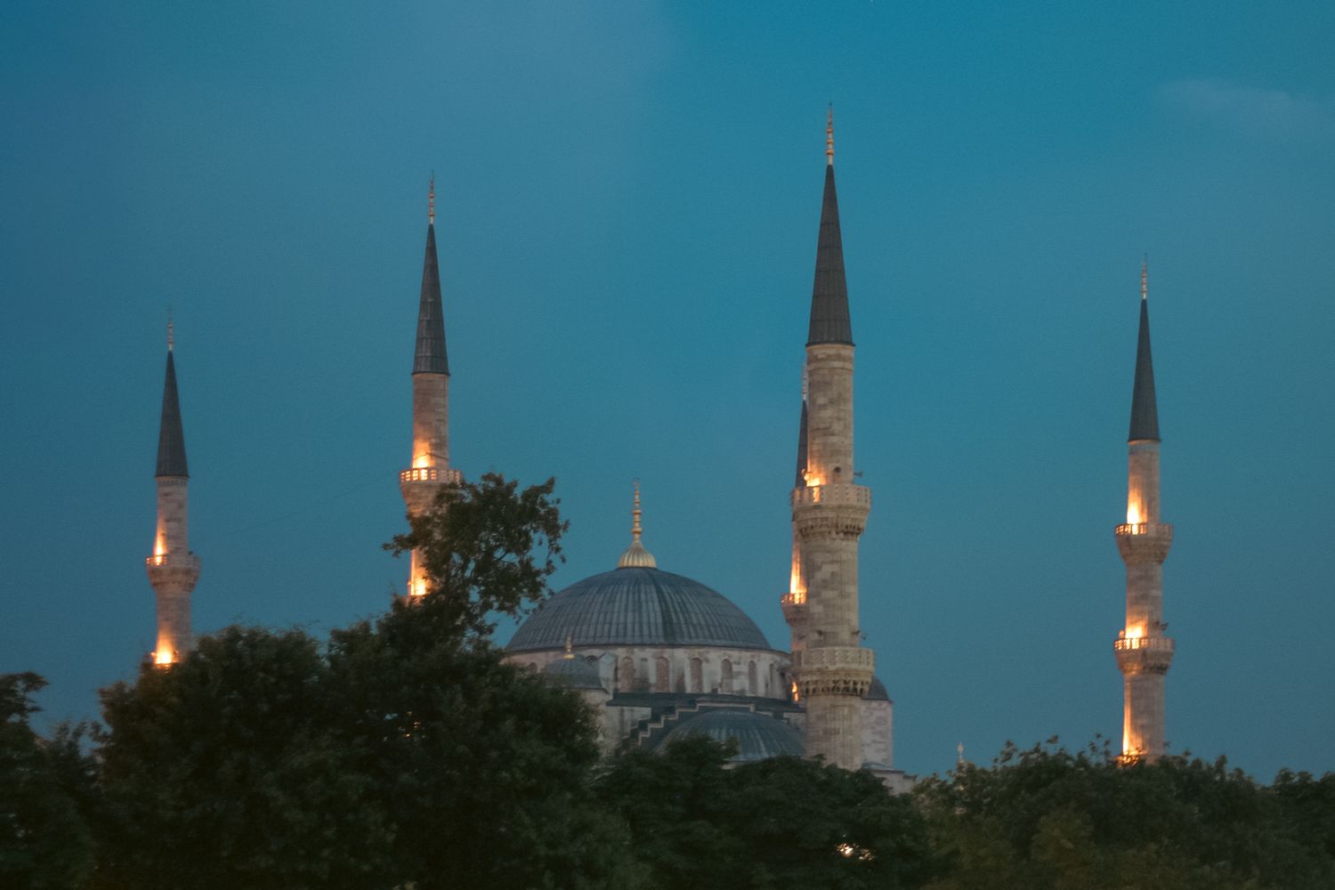 Istanbul's Blue Mosque minarets and domes silhouetted against twilight sky with illuminated spires.