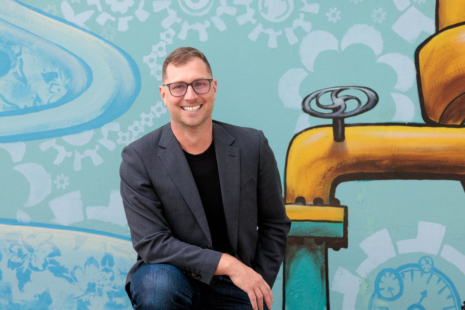 Person seated against colorful mural wall with whimsical design elements.