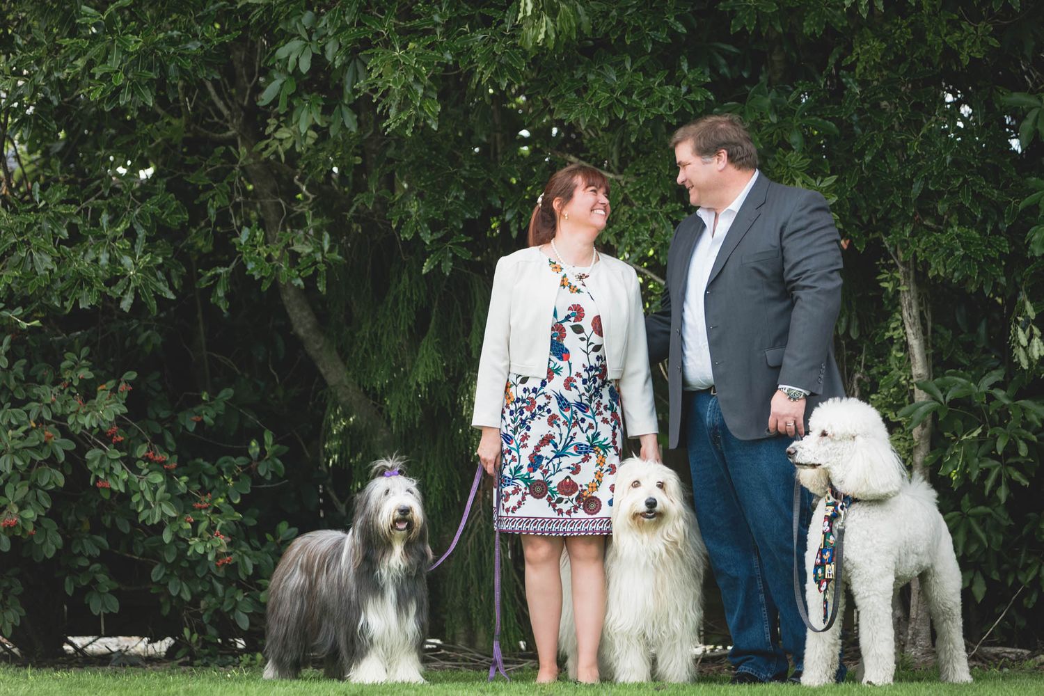 A couple poses with their dogs among lush greenery during an outdoor photo session.