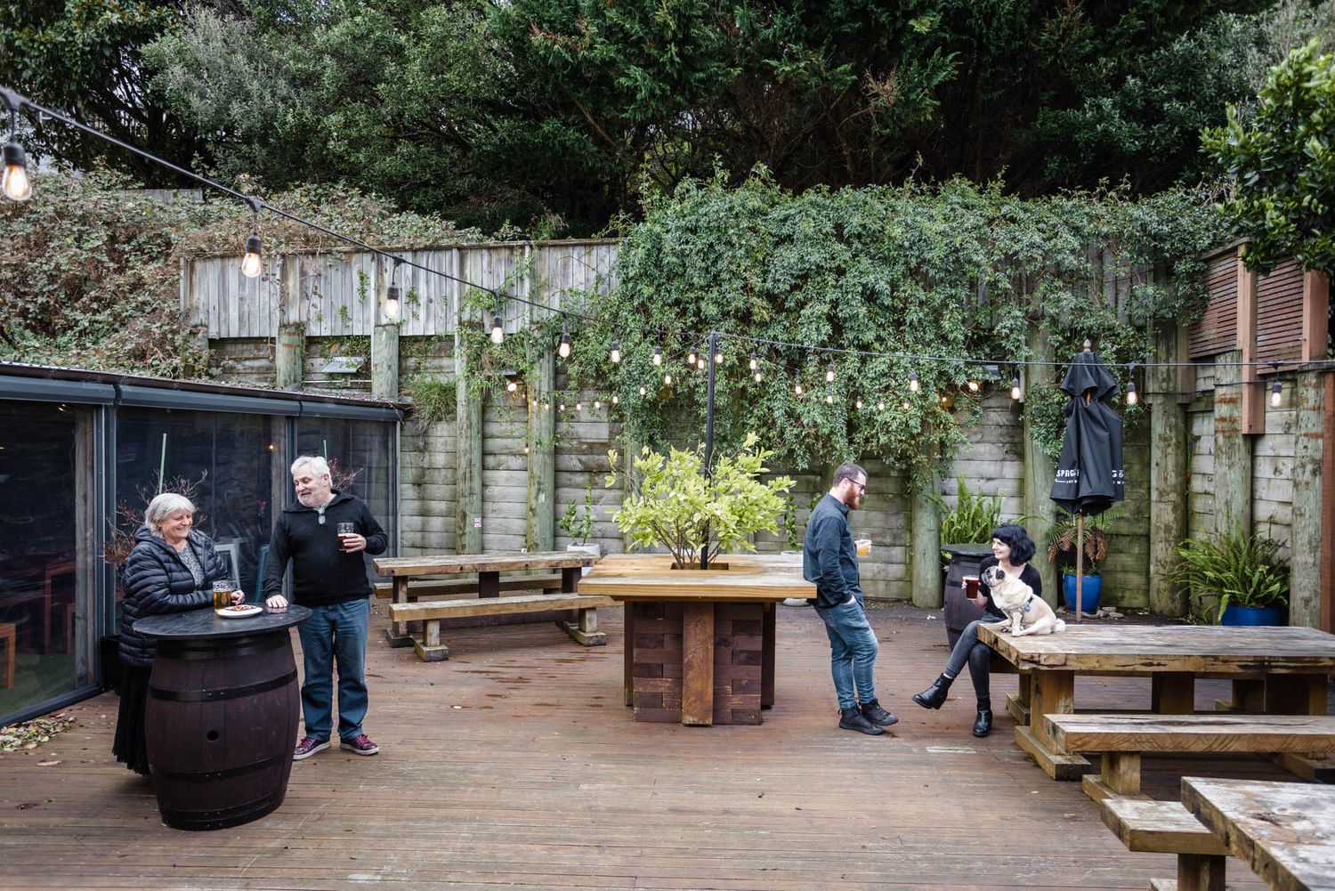 Outdoor beer garden seating area with wooden benches and lush greenery.