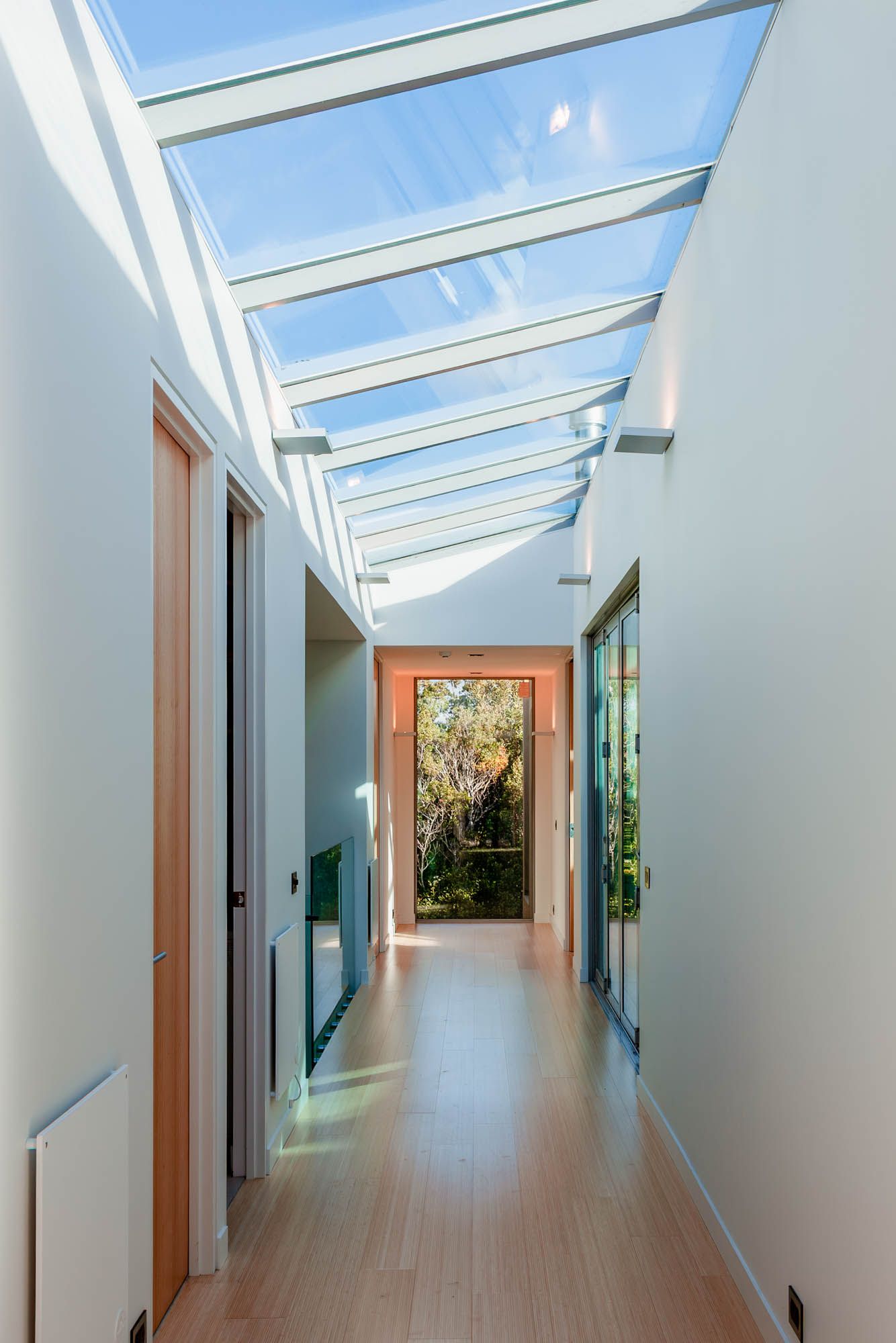 Minimalist white corridor with skylights creating natural light patterns along wooden flooring.